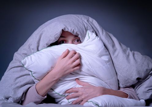 Young girl hugs a pillow and hid under a blanket from all problems, procrastinating, millennials generation. Woman covered with a blanket and is worried about insomnia, poor sleep, getting stress.