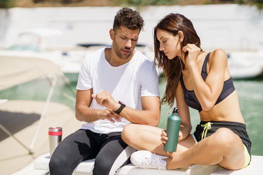 Man showing his marks to an athletic woman on a sports watch after exercise. People using smartwatch.