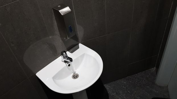 white ceramic washbasin with chrome faucet in the toilet with gray tile.