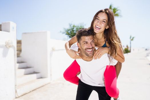 Man carrying his girlfriend on piggyback wearing sportswear. Couple having fun together.