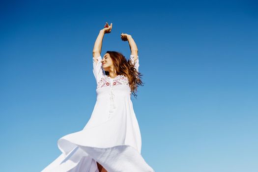 Young beautiful woman raising her arms in a beautiful white dress in Spanish fashion against a blue sky in nature