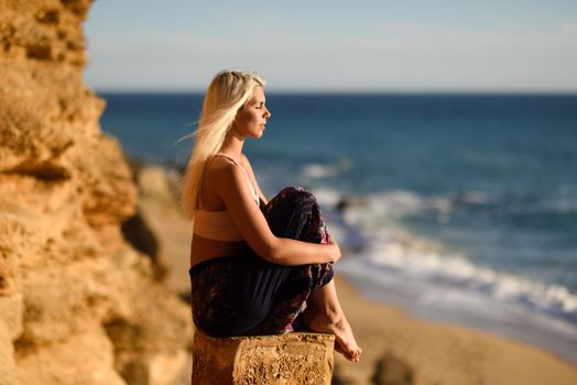 Woman enjoying the sunset on a beautiful beach in Cadiz, Andalusia, Spain. Young female sitting on beautiful stairs looking at the sea with golden light.