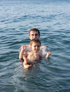 Happy family and healthy lifestyle. A young father teaches a child to swim in the sea
