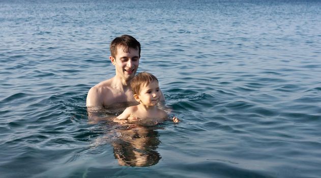 Happy family and healthy lifestyle. A young father teaches a child to swim in the sea