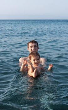 Happy family and healthy lifestyle. A young father teaches a child to swim in the sea