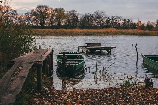 A boat near the river shore filled with water and golden autumn leavesin sunset time.