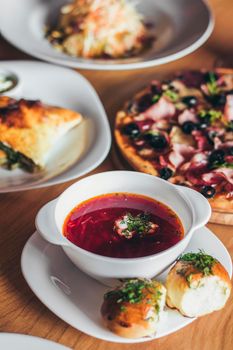Ukrainian and russian national red borsch with buns and other dishes served on the table.