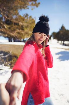 Blonde woman in winter clothes walking holding her partner's hand in the snowy mountains., in Sierra Nevada, Granada, Spain.