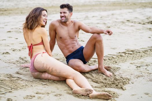 Young couple of beautiful athletic bodies sitting together on the sand of the beach enjoying their holiday at sea