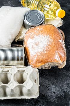 Kitchen table with Donation food goods, quarantine help concept. Oil, canned food, pasta, bread, sugar, egg. Black background. Top view.