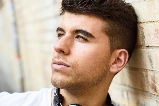 Close-up portrait of a young man with blue eyes posing near a wall. Model of fashion in urban background wearing white t-shirt