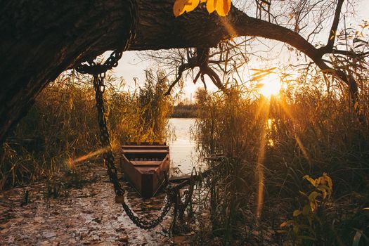 A boat near the river shore filled with water and golden autumn leavesin sunset time.