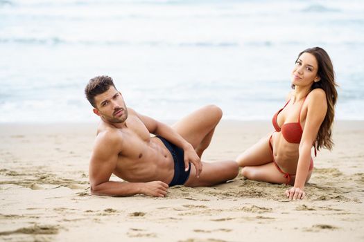 Young couple of beautiful athletic bodies sitting together on the sand of the beach enjoying their holiday at sea