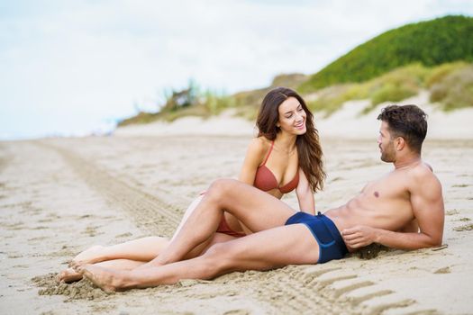 Young couple of beautiful athletic bodies sitting together on the sand of the beach enjoying their holiday at sea