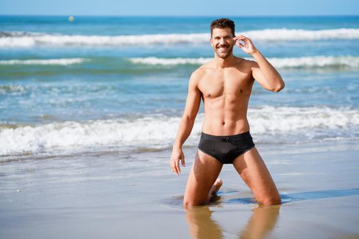 Attractive man on his knees smiling on the sand of the beach