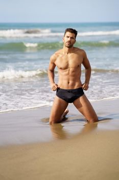 Attractive man on his knees on the sand of the beach