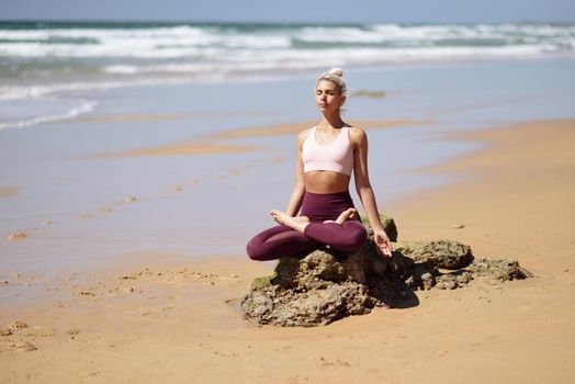 Caucasian woman practicing yoga at seashore. Young female doing lotus pose in the beach in Cadiz, Andalusia, Spain.