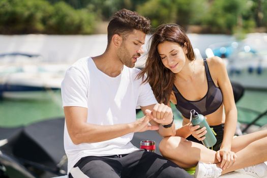 Man showing his marks to an athletic woman on a sports watch after exercise. People using smartwatch.