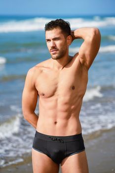 Young athletic man with fitness body standing on the sand of the beach