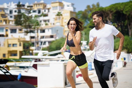 Young athletic couple training together running near the boats in a harbour