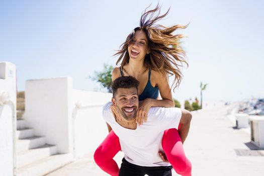 Man carrying his girlfriend on piggyback wearing sportswear. Couple having fun together.