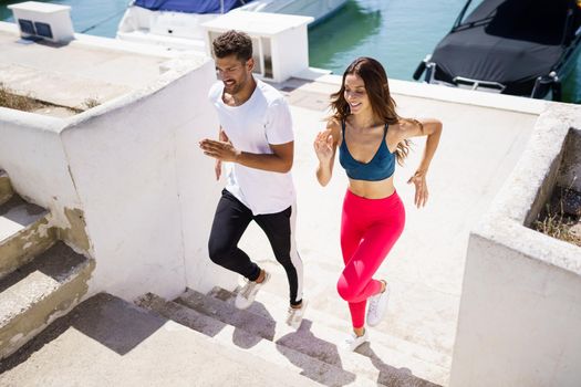 Athletic couple training hard by running up stairs together near the boats in a harbour