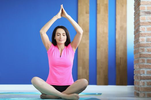 Portrait of young smiling woman practicing yoga position on mat in comfy outfit. Light studio for training and meditation. Healthcare, wellness, peace of mind concept