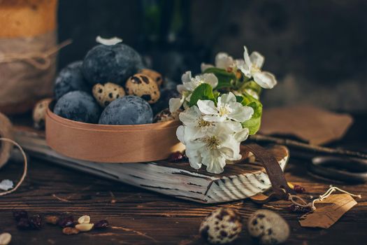 Easter eggs in the round wooden box on rustic wooden background with apple blossom branch