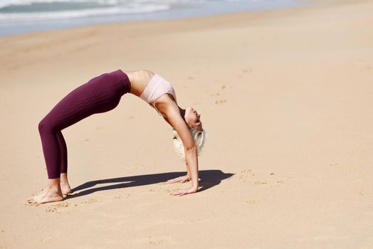 Caucasian woman practicing yoga at seashore. Young female standing in bridge pose in the beach in Cadiz, Andalusia, Spain.