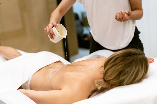 Beauty salon professional pouring oil from a massage candle on the back of his female patient.