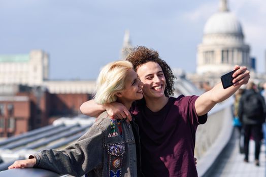 Happy couple taking a selfie photograph on London's Millennium Bridge, River Thames