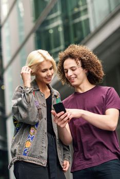 Happy couple using smartphone in urban background. Young man and woman wearing casual clothes in a London street.