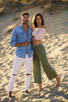 Young couple standing on the sand of the beach wearing casual clothes.