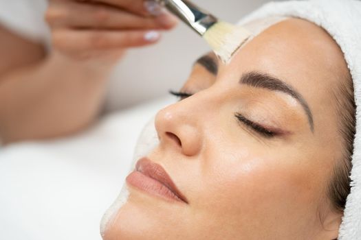 Aesthetics applying a mask to the face of a Middle-aged woman in modern wellness center. Beauty and Aesthetic concepts.