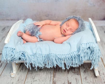 lovely newborn boy sleeping on little bed with blue diaper in hat and panties