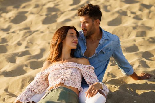 Happy loving couple sitting on the sand of the beach enjoying each other