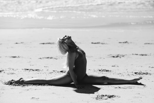 Caucasian woman practicing yoga at seashore. Young female doing fitness legs split on sand in the beach in Cadiz, Andalusia, Spain.