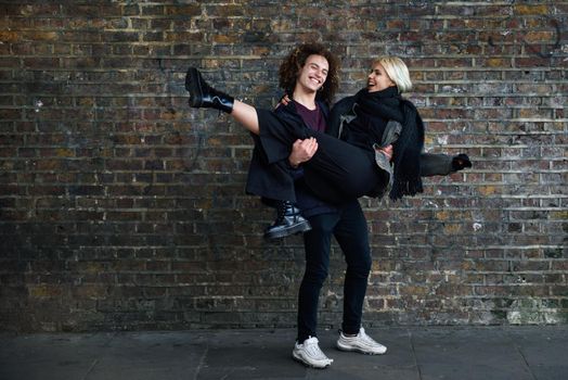 Man holding his girlfriend in his arms. Young couple enjoying Camden town in front of a brick wall typical of London, UK