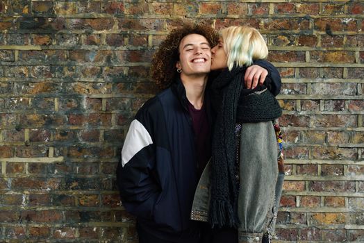 Young couple enjoying Camden town in front of a brick wall typical of London, UK. Man and woman kissing