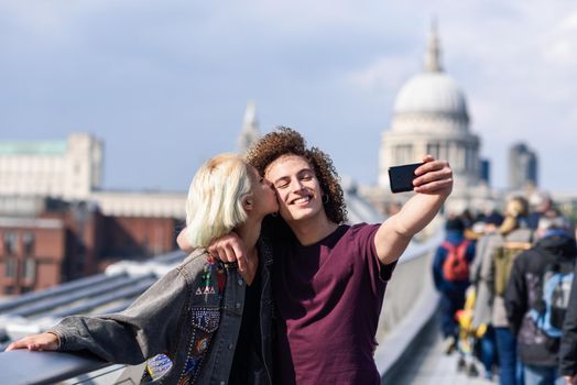 Happy couple taking a selfie photograph on London's Millennium Bridge, River Thames