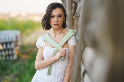 Pretty young Asian woman, posing near a tobacco drying shed, wearing a white dress and green wellies. Beauty and fashion concept