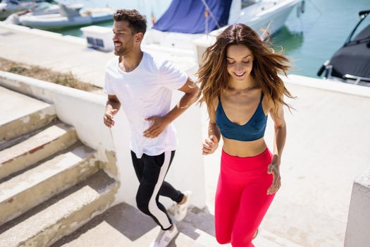 Athletic couple training hard by running up stairs together near the boats in a harbour