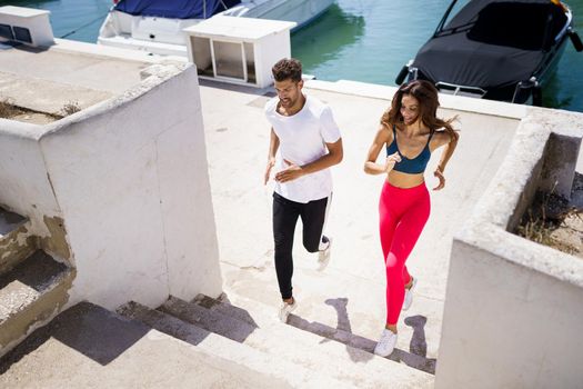 Athletic couple training hard by running up stairs together near the boats in a harbour