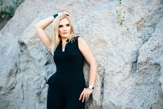 blonde girl in a black trouser suit with blue eyes on the background of a granite quarry from gray rubble