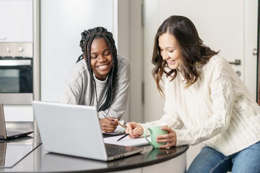 Two college girls studying together at home with laptops while drinking coffee. Multiethnic women.