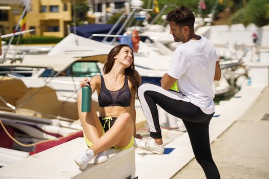 Young fitness man and woman hydrate themselves with water in metal bottles while taking a break after sport.