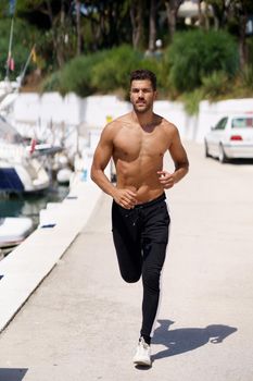 Young man with an athletic body running shirtless through a harbour full of boats.