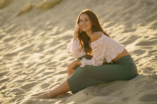 Smiling woman sitting on the sand of the beach looking at the horizon.