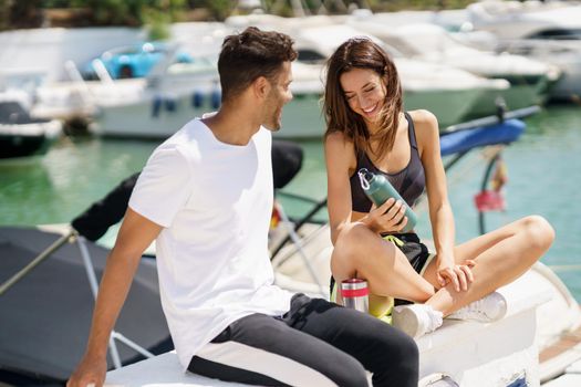 Young sporting couple hydrate themselves with water in metal bottles while taking a break after sport.