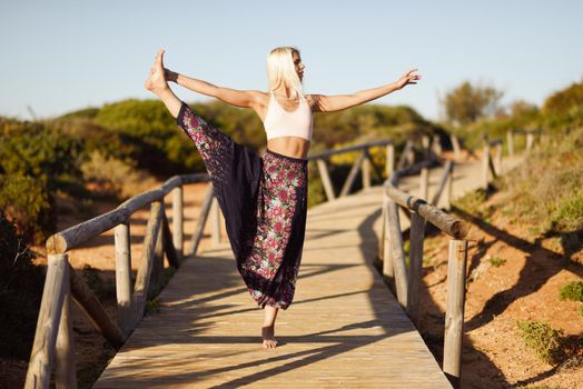 Woman enjoying the sunset on a beautiful beach in Cadiz, Andalusia, Spain. Caucasian female practicing yoga on wooden bridge.